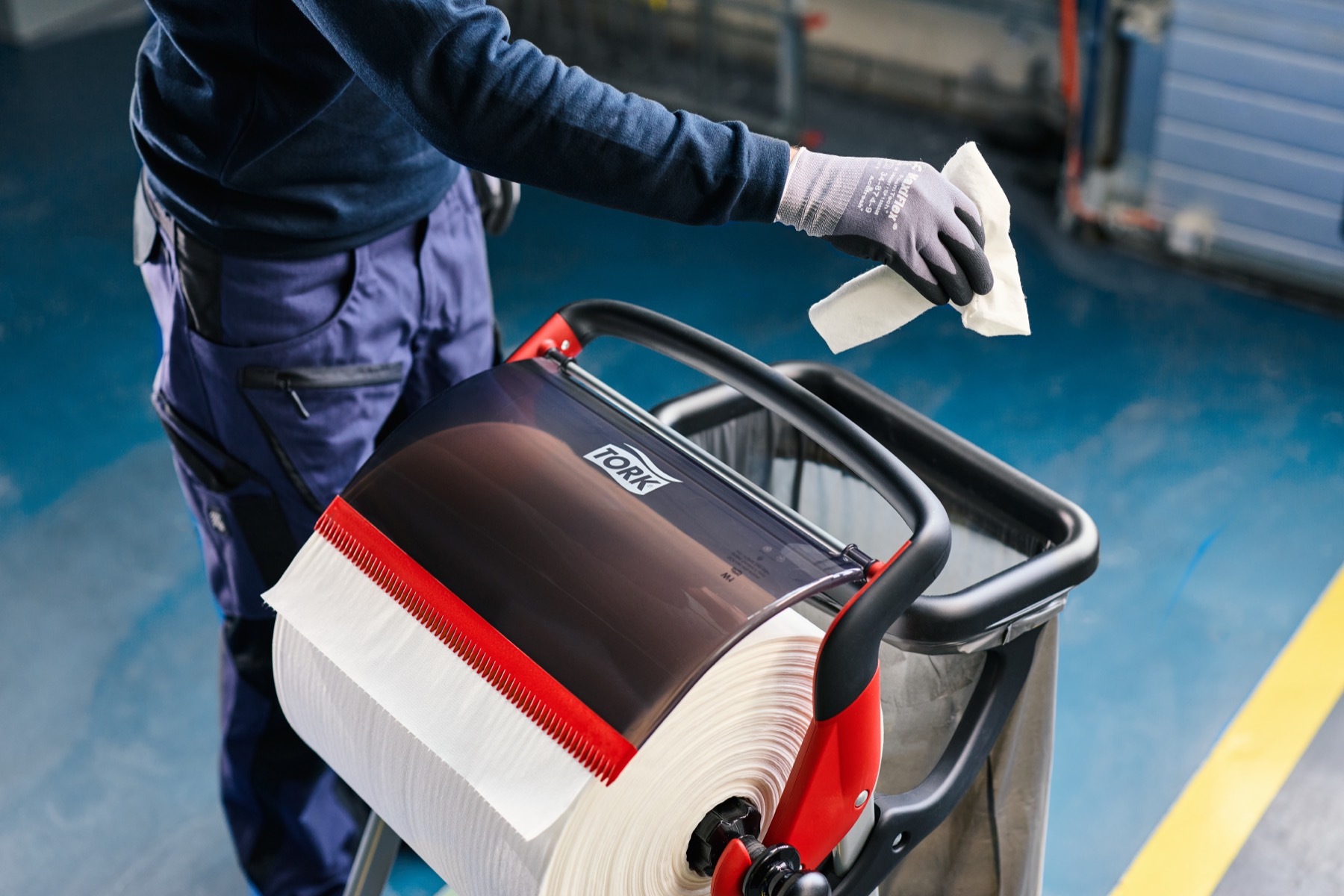 Handen pakken een poetsdoek uit een Tork-dispenser op een schoonmaaktrolley